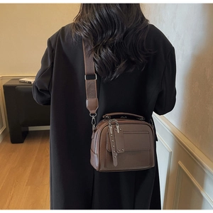 Detailed close-up of a vintage dark brown leather crossbody bag with wide canvas strap