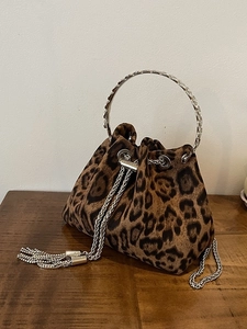Fashionable leopard print bucket bag with metal handle and chain strap on wood