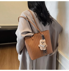 Dettaglio di una borsa tote intrecciata marrone con un simpatico ciondolo a forma di orso