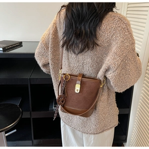 Brown quilted bucket bag with gold clasp shown worn on shoulder in minimalist setting