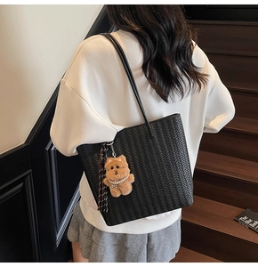 Detail of black woven texture tote bag featuring plush bear and leather tassel charms