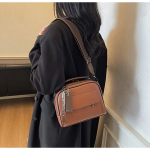 Detail of brown litchi pattern leather shoulder bag with adjustable wide strap and rivet trim