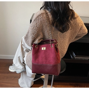 Close-up of burgundy suede bucket bag with quilted patterns and golden chain strap