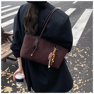 Outdoor view of a dark coffee tote bag with quilted stitching and beaded charm accessory