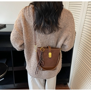 Detailed view of brown quilted bucket bag with gold clasp and tassel charm on model