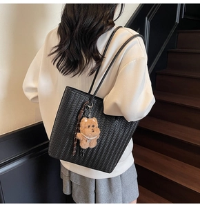 Detail of black woven tote bag with brown plush bear pendant shown on model shoulder