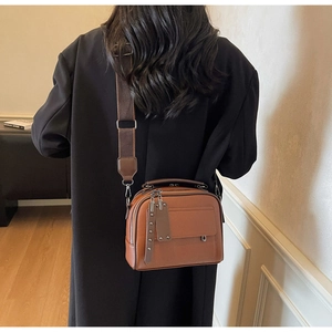 Close-up of brown litchi pattern leather camera bag with wide fabric strap on a black coat