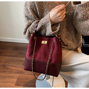 Detail of burgundy suede and leather bucket bag with quilted patterns and gold twist lock