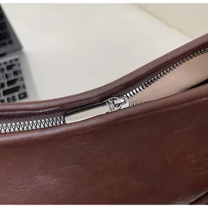 Detail view of the smooth silver metal zipper on a dark brown leather underarm bag