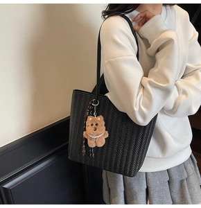 Close-up of black woven tote bag with leather strap and cute brown plush bear charm