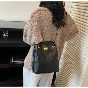 Detalle de un bolso cubo acolchado negro con correa de cadena llevado al hombro