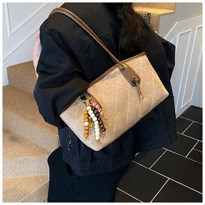 Detail of beige quilted shoulder bag with bohemian colorful wooden beaded pendant