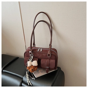 Detail view of burgundy faux suede Boston bag with two pockets and teddy bear charm
