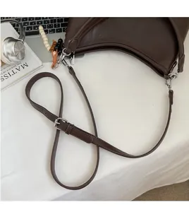 Detail of adjustable long shoulder strap and silver metal buckle on brown hobo bag