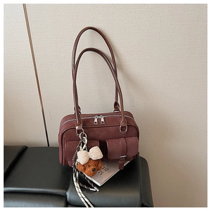 Detail of burgundy Boston shoulder bag with dual buckled pockets and cute bear charm