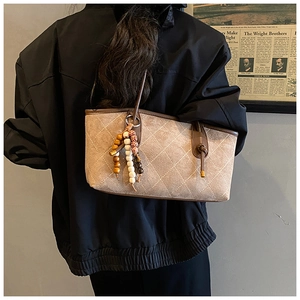Quilted khaki tote bag with ethnic beaded charm shown on model in a retro setting