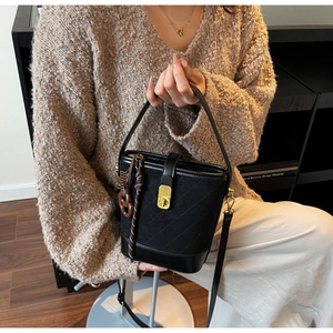 Detail of black quilted bucket bag with gold hardware and twisted cord charm accent