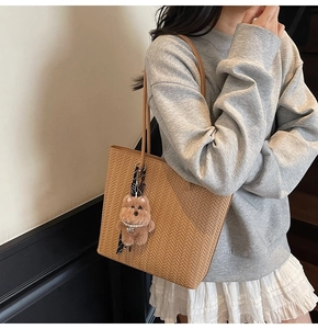 Dettaglio della borsa tote intrecciata marrone con ciondolo a cucciolo e collana di perle
