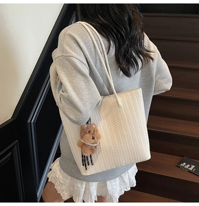 Dettaglio di una borsa tote intrecciata bianca con un simpatico ciondolo a forma di orsetto