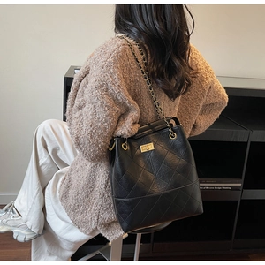 Detail of black quilted bucket bag with golden chain strap and twist lock closure