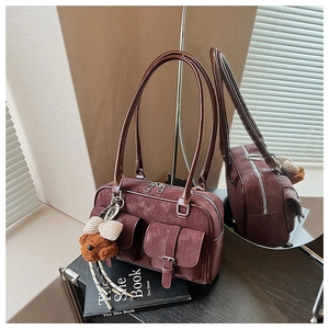 Detail of reddish brown suede shoulder bag with dual pockets and a plush bear charm