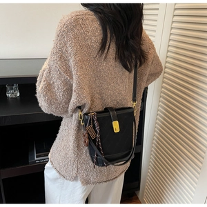 Detail view of a matte black bucket bag with a golden turn-lock and vintage abacus charm