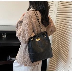 Detail of black quilted bucket bag with gold chain strap and turn-lock closure