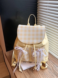 Chic yellow patchwork backpack with plaid flap and lace bows on a wooden table