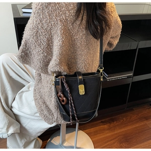 Detail of black quilted bucket bag featuring a golden twist lock and decorative charm