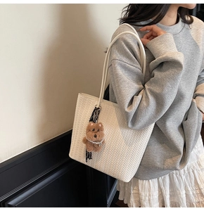 Dettaglio borsa tote bianca intrecciata con ciondolo a forma di orsetto e perline