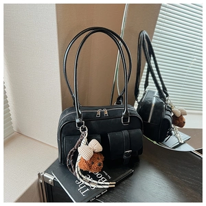 Detail view of black suede Boston bag with shiny leather trim and teddy bear charm