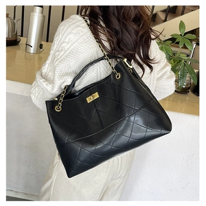 Detailed view of the large quilted tote bag with gold chain strap worn by a model