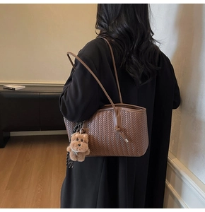Détail d'un sac cabas tissé marron avec texture en V et un pendentif ours en peluche