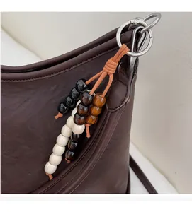 Detail of a brown leather shoulder bag with a stylish wooden beaded keychain and silver ring