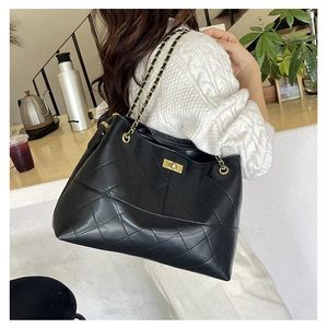 Detail of black quilted tote bag featuring golden chain strap and turn-lock closure