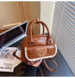 Detail of a brown PU leather handbag featuring a cute plush bear and white lace trim