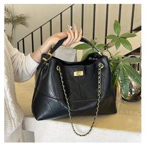 Detail of black quilted faux leather tote bag with gold chain strap and metal buckle