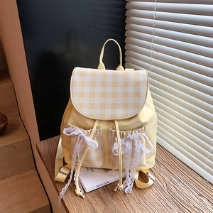 Yellow preppy backpack with checkered flap and white lace bows on a wooden surface