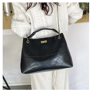 Close-up of quilted black suede tote bag with golden chain strap and twist lock detail