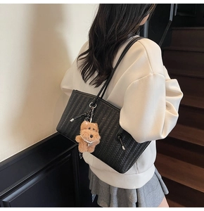 Détail d'un sac cabas tissé noir avec breloque chiot en peluche sur un modèle minimaliste