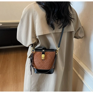 Detail of a brown quilted bucket bag with gold hardware worn by a model in a minimal setting
