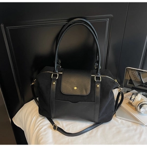 Détail du sac cabas noir mat avec patchwork de cuir et garnitures dorées sur lit blanc