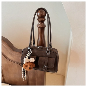 Detail of dark brown suede Boston bag with dual pockets and plush teddy bear charm