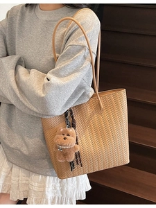 Borsa tote in pelle intrecciata kaki con ciondolo a orsetto su sfondo di scale in legno