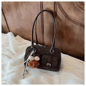 Detail of vintage brown suede shoulder bag with twin buckle pockets and teddy bear charm