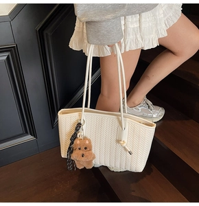 Détail d'un cabas tressé blanc avec charm ours en peluche marron sur des escaliers