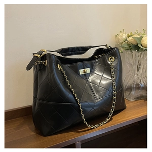 Detail of black quilted tote bag with gold twist-lock closure and metal chain strap