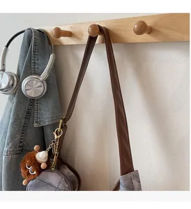 Detail of grey denim bag with brown leather strap and plush animal pendant on wood hook