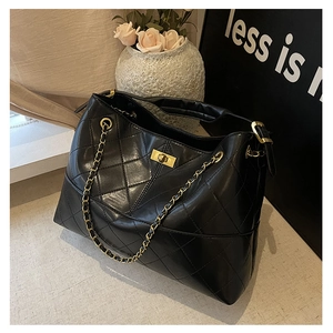 Detail of black quilted shoulder bag featuring gold chain and turn-lock metal closure