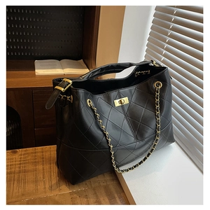 Detail of black quilted tote bag with gold chain strap and twist lock on a windowsill